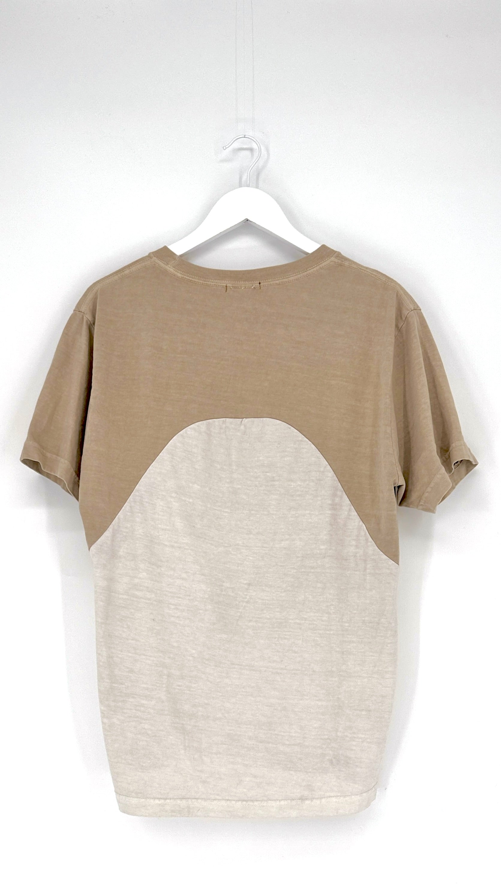 Two-tone t-shirt with beige and white design on a hanger against a white background